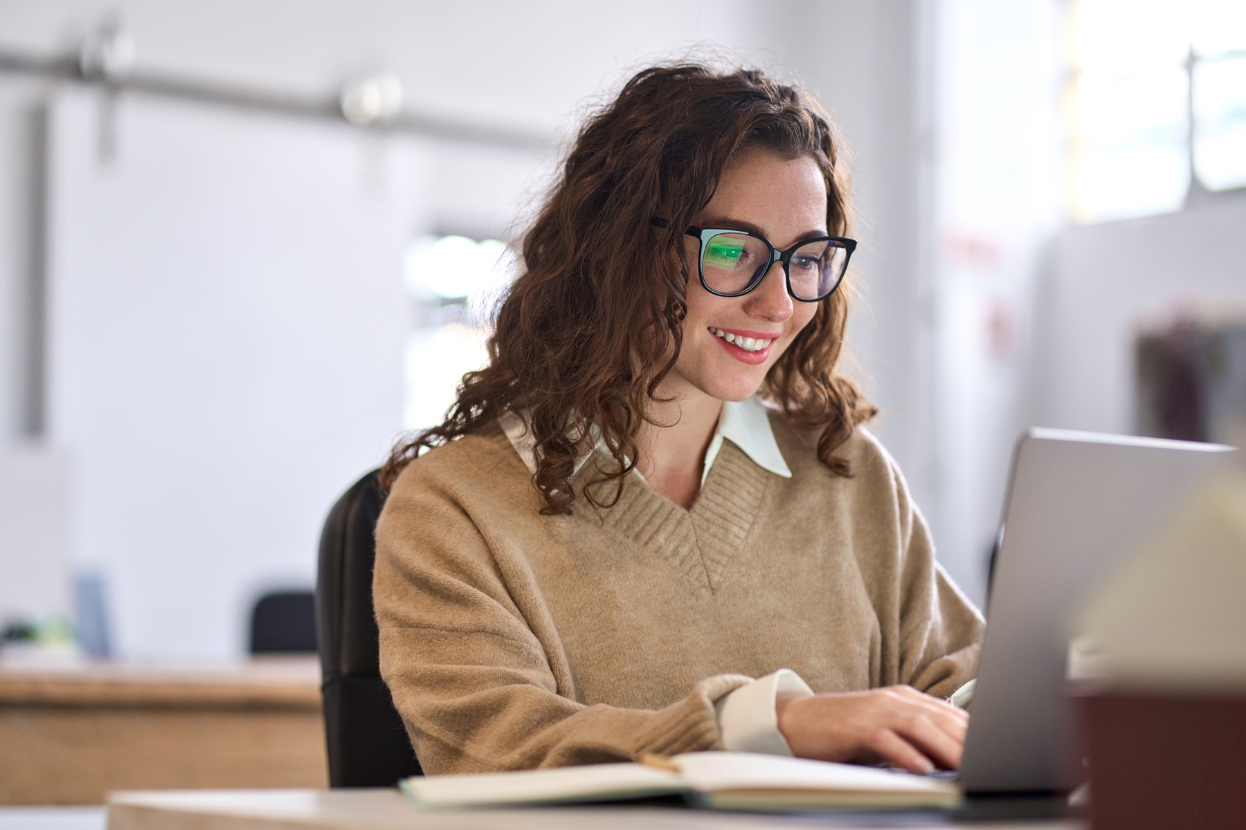 Young happy professional business woman worker employee sitting at desk working on laptop in corporate office